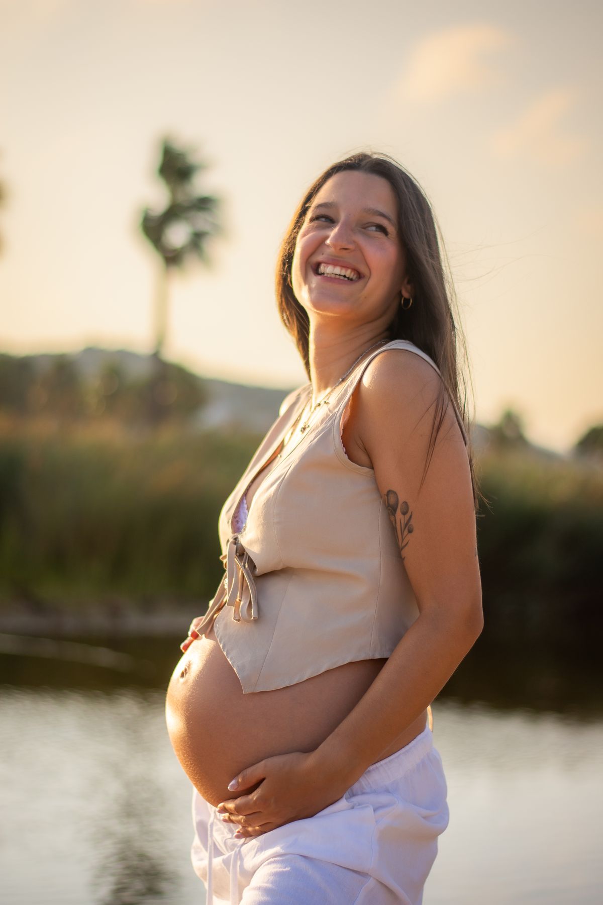 Mujer embarazada sonriente al atardecer junto a una palmera